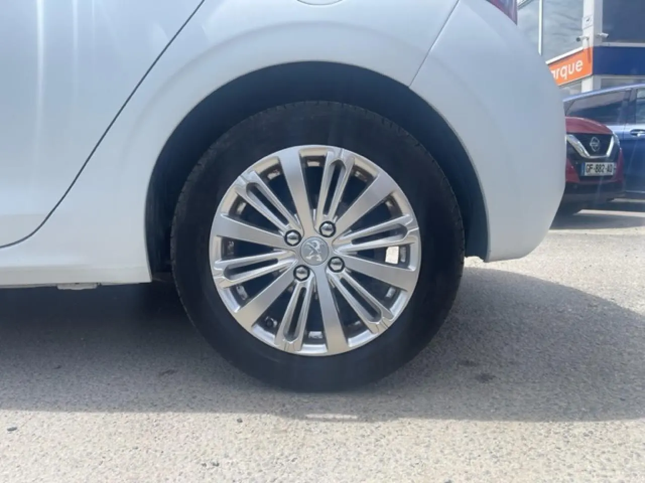 Gros plan sur la jante alliage 16 pouces Titane Technical Grey côté arrière droit d'une Peugeot 208 blanc perle texture.