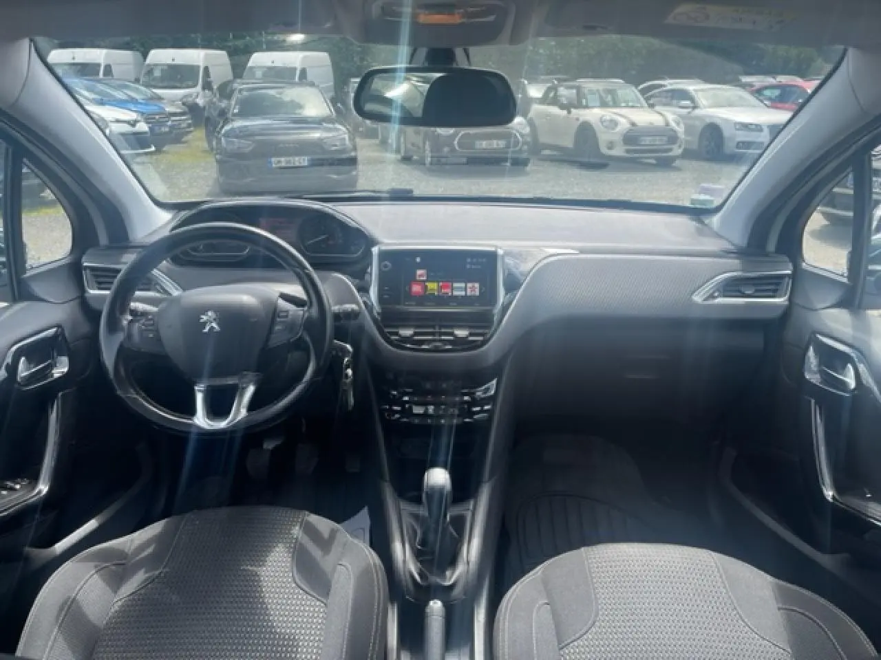 Vue intérieure avant de la Peugeot 208 blanche perle, montrant le volant compact multifonction et l’écran tactile central.