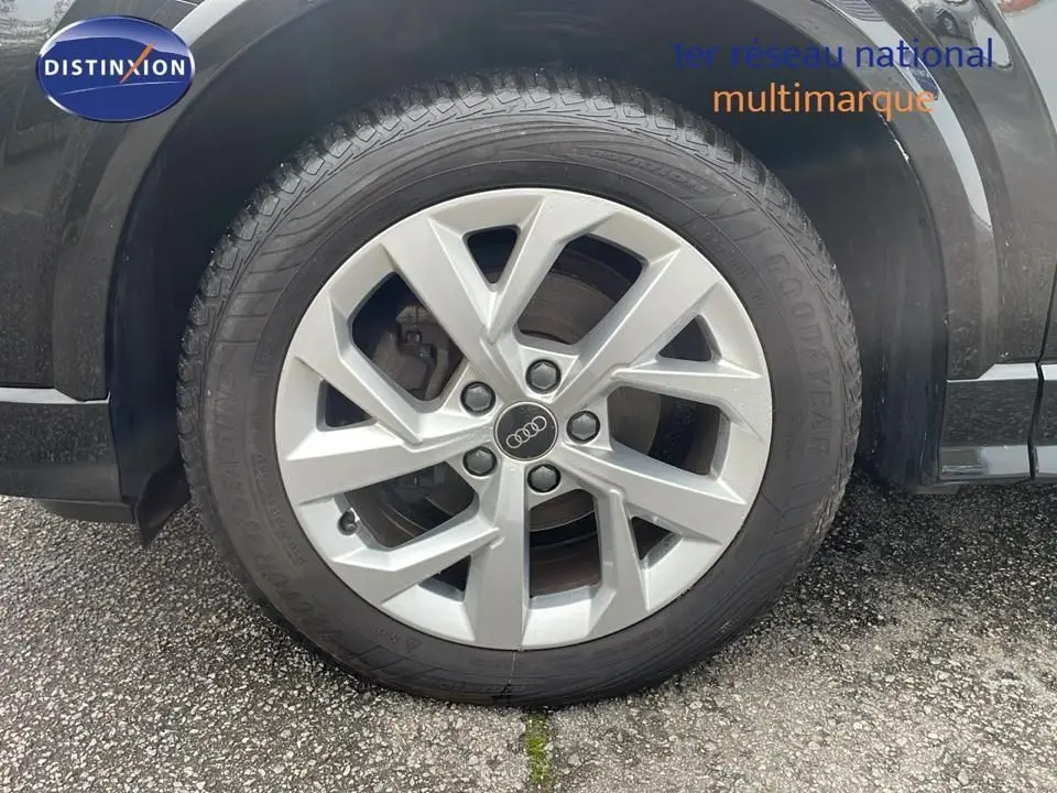 Gros plan sur la roue avant gauche d'un Audi Q2 noir mito metal avec jante alliage 17 pouces et logo Audi central.