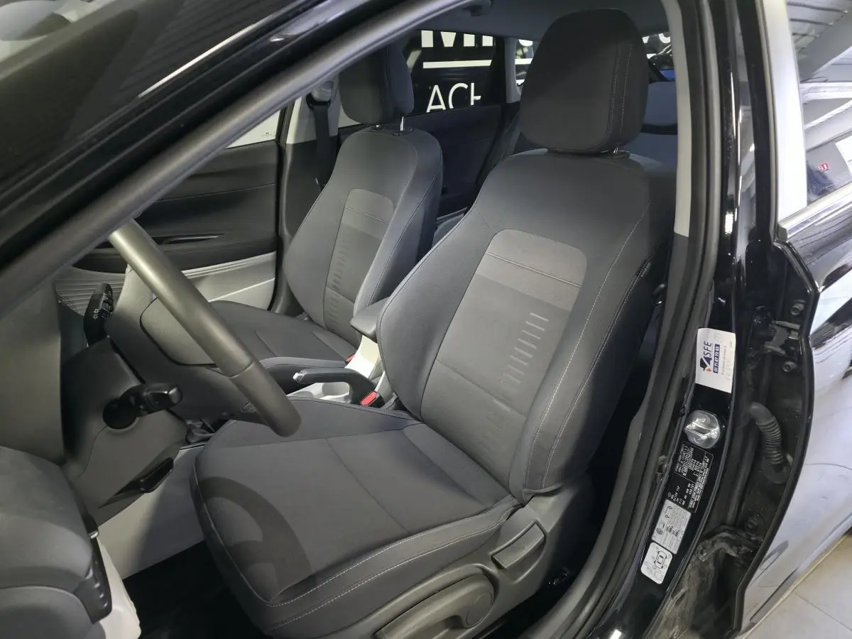 Vue intérieure côté conducteur du Hyundai Bayon noir 2025, sièges tissu gris et accoudoir central coulissant visible.