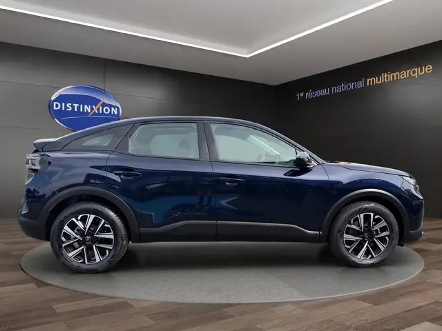 Vue latérale droite d'une Citroën C4 hybride 2025 bleu foncé avec jantes alliage et toit noir dans un showroom.