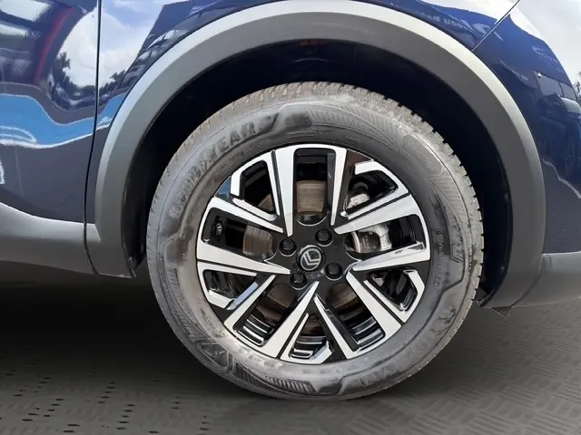 Gros plan sur la roue avant droite d'une Citroën C4 hybride bleue avec jante alliage bicolore et pneu Goodyear.