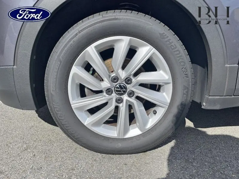 Gros plan sur la roue avant gauche du Volkswagen T-cross gris cendré avec jante alu et logo VW au centre.