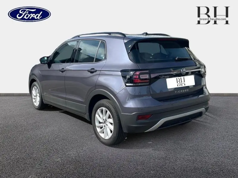 Volkswagen T-Cross gris cendré métallisé vu en 3/4 arrière droit avec barres de toit et jantes alu visibles.
