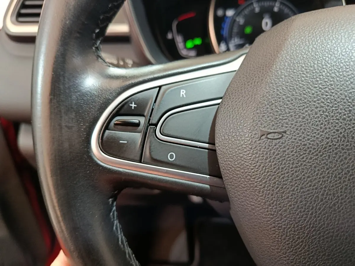 Gros plan sur les commandes de régulateur de vitesse au volant cuir du Renault Kadjar Intens rouge, tableau de bord flou en arrière-plan.