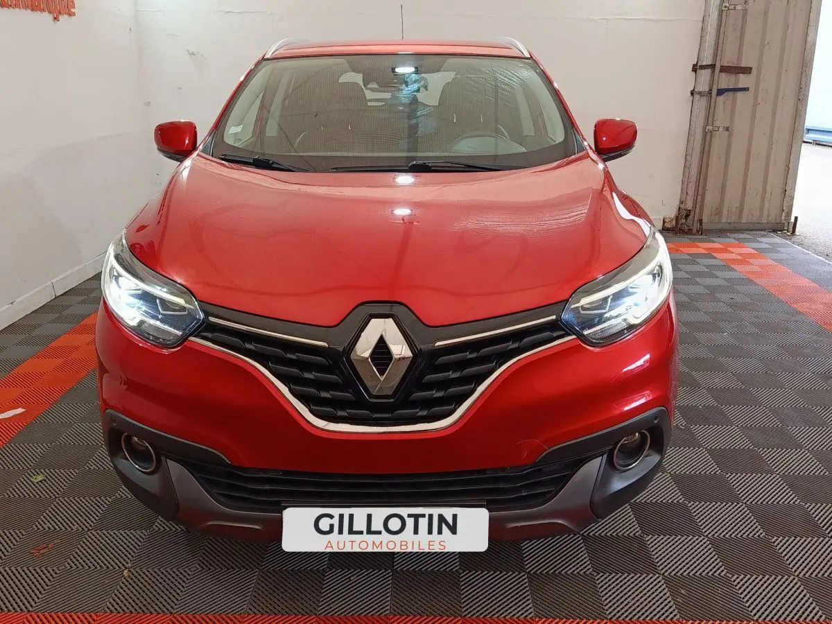 Vue avant d'un Renault Kadjar rouge avec phares LED allumés dans un garage au sol carrelé noir et orange.