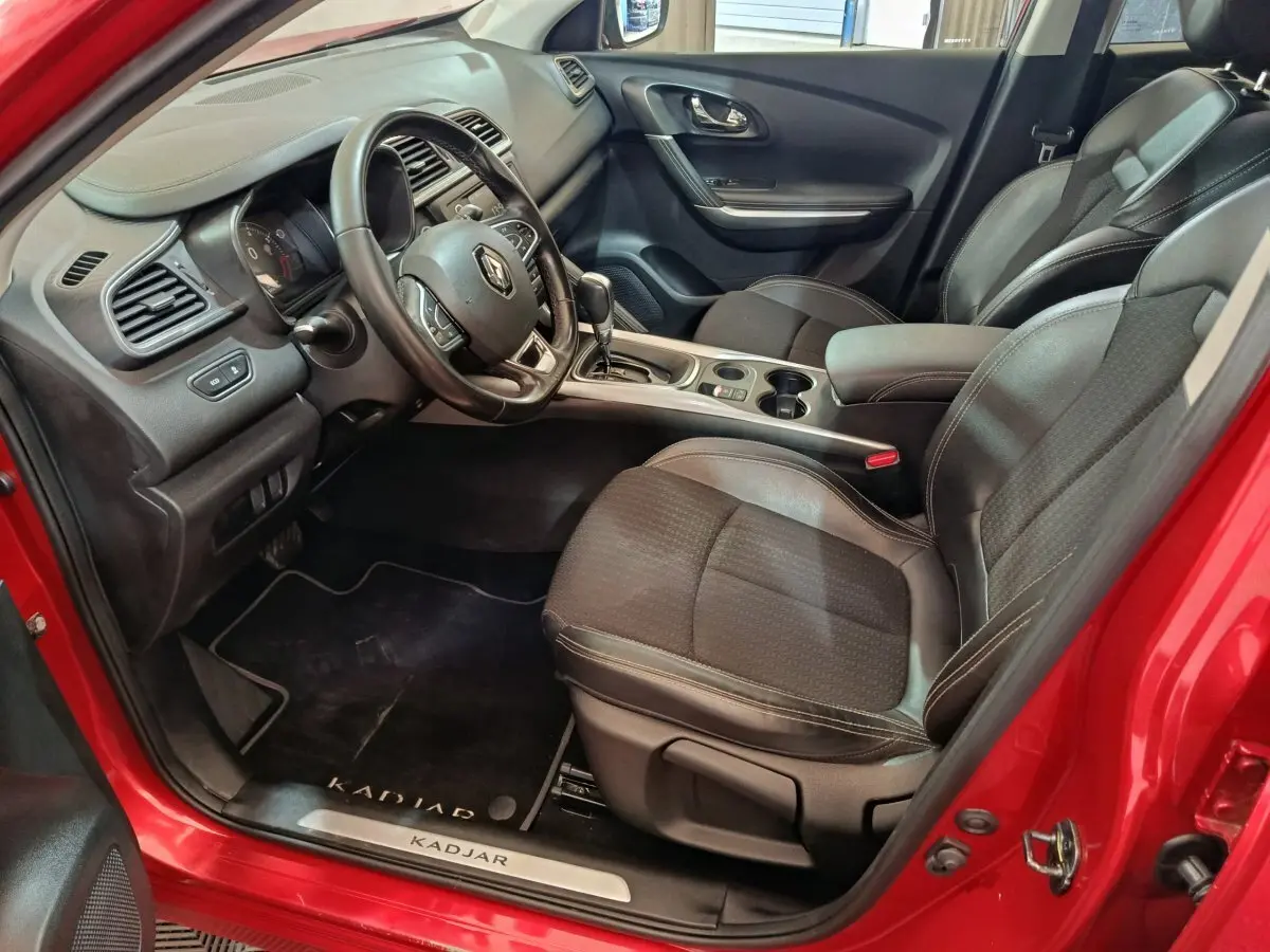 Vue intérieure côté conducteur du Renault Kadjar rouge, montrant le volant cuir multifonctions et les sièges noirs.