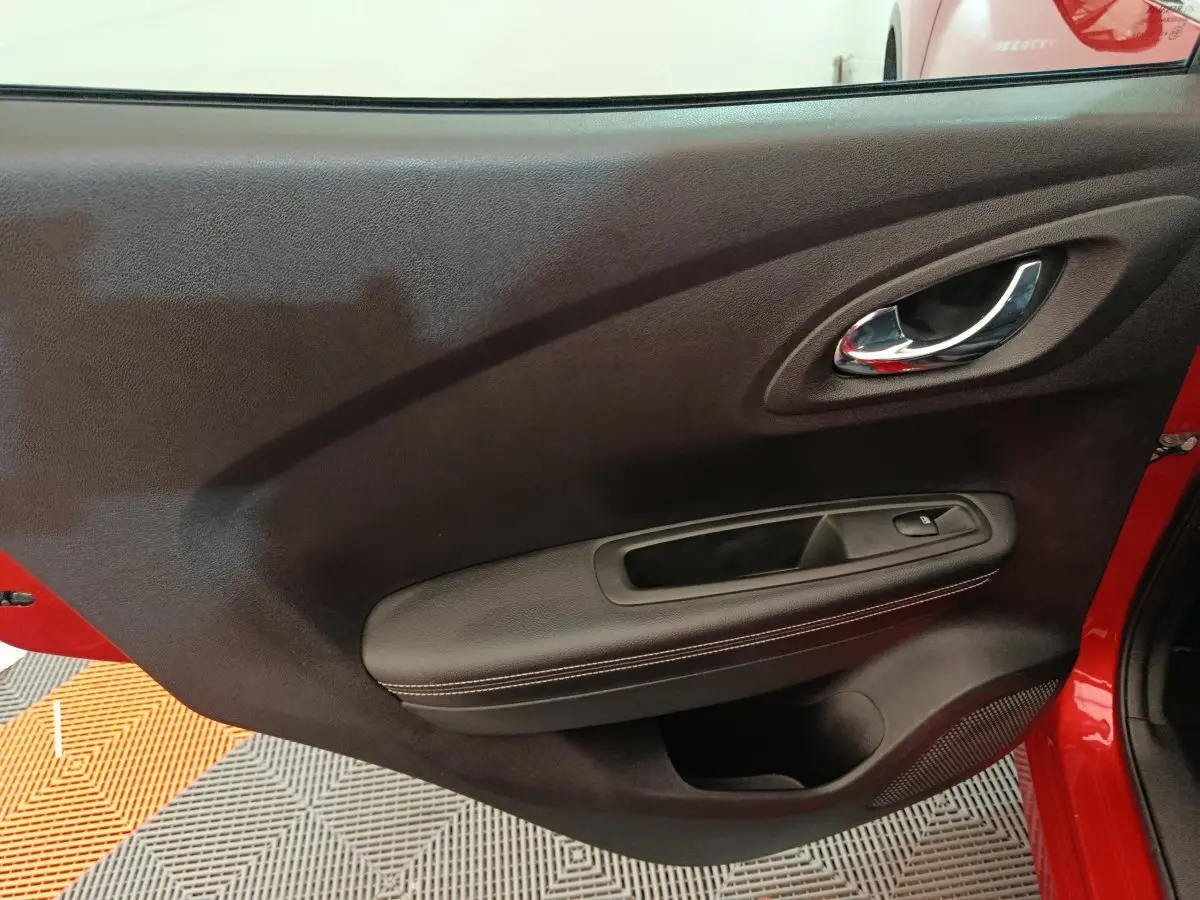 Gros plan sur la porte intérieure côté gauche du Renault Kadjar rouge, avec poignée chrome et accoudoir noir.