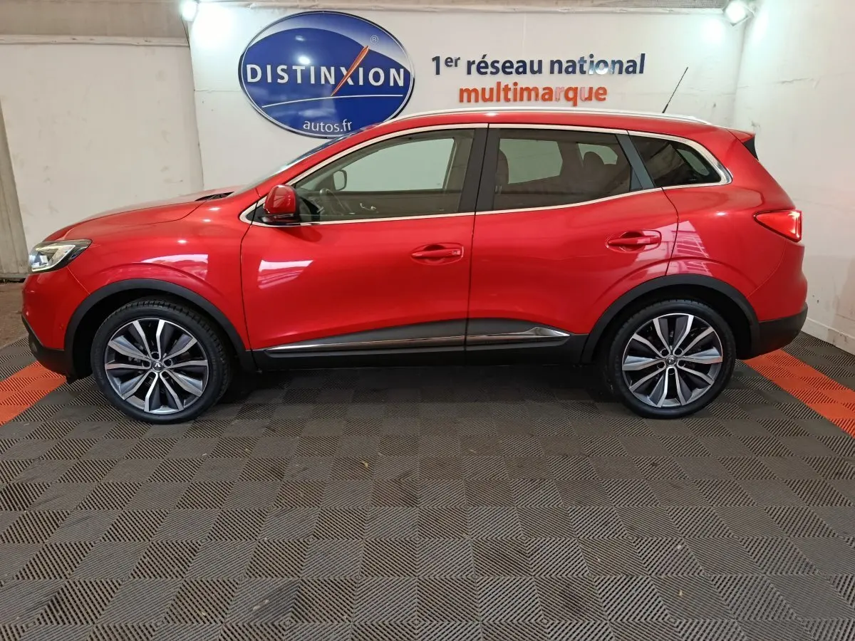 Profil côté gauche du Renault Kadjar rouge Intens Energy TCe 130 EDC avec jantes alliage et rails de toit chromés.