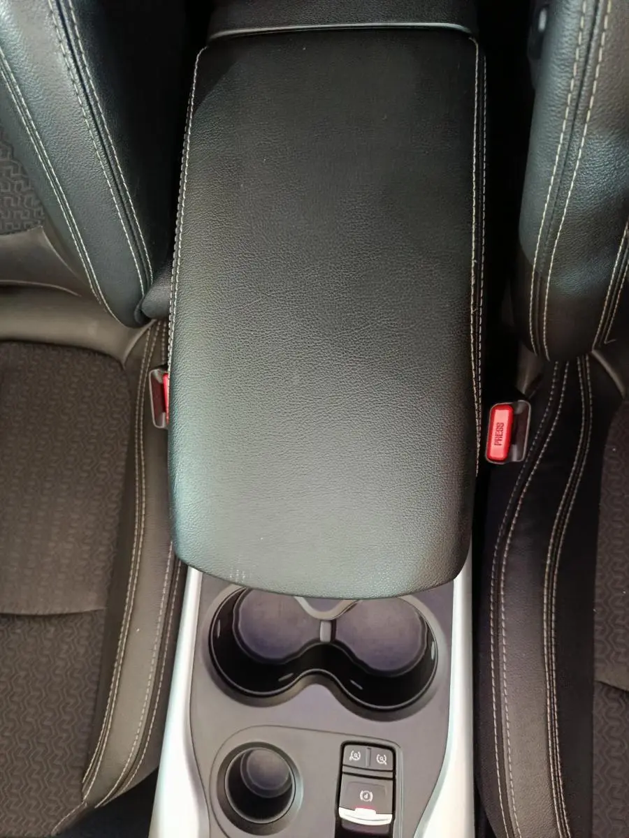 Vue plongeante sur la console centrale noire en cuir avec accoudoir et porte-gobelets du Renault Kadjar Intens rouge.