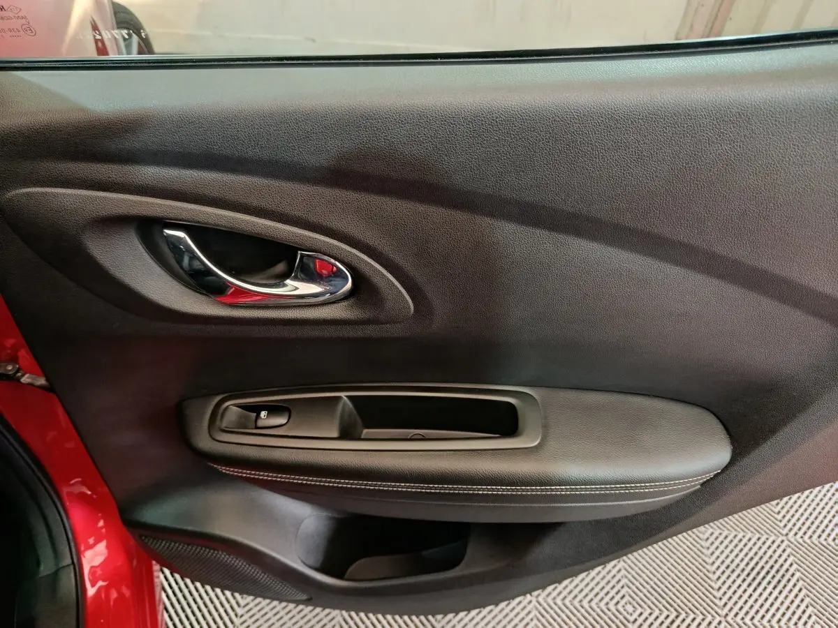Intérieur côté gauche de la porte rouge Renault Kadjar Intens, avec poignée chrome et commande de vitre noire.