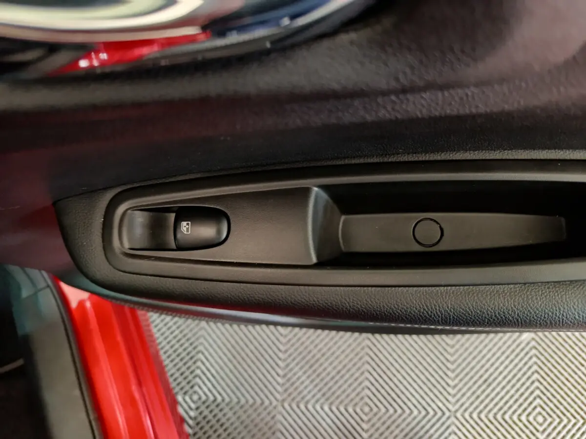 Gros plan sur la commande de lève-vitre côté conducteur d’un Renault Kadjar rouge visible à l’ouverture de la porte.