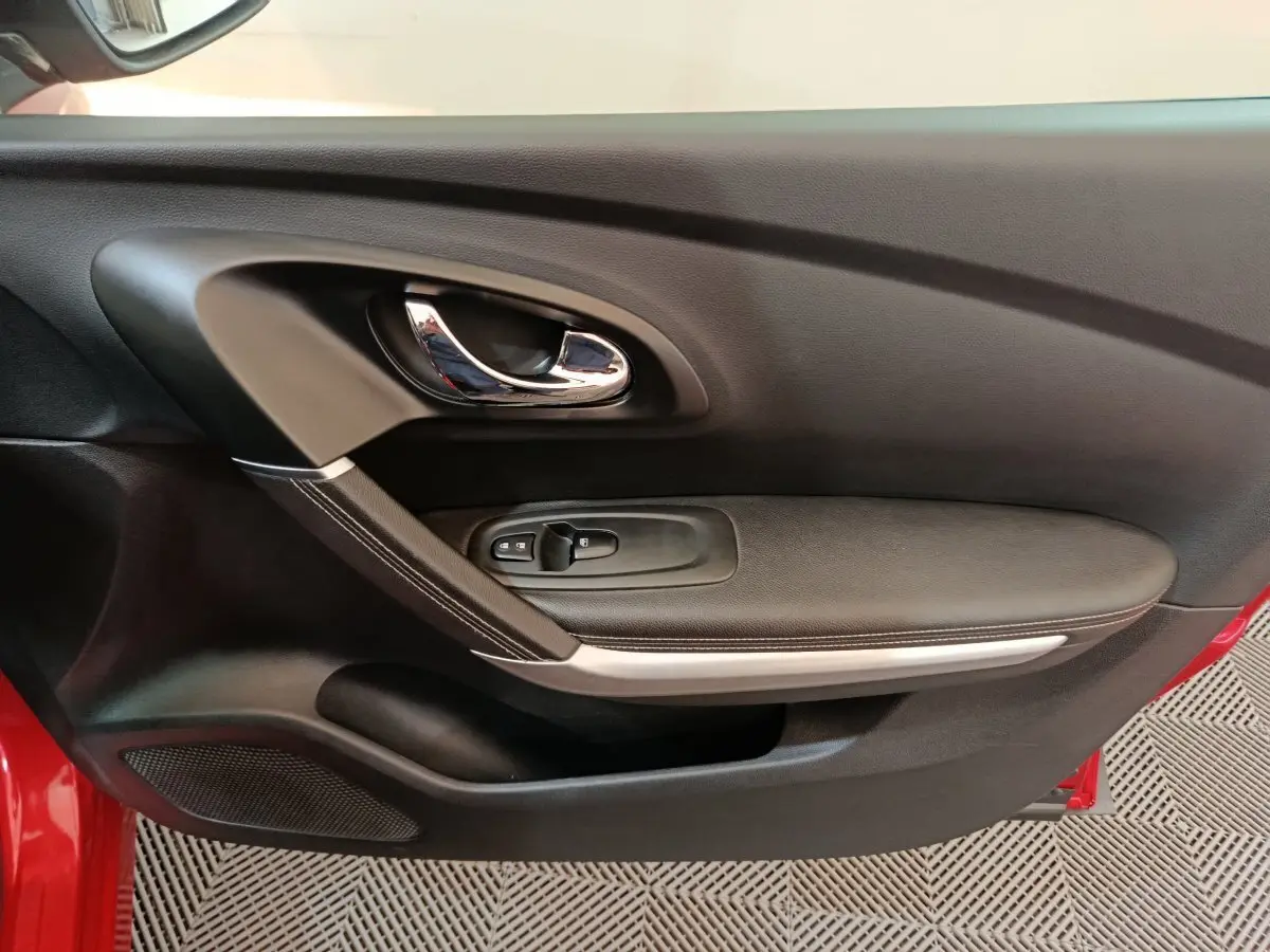 Gros plan sur la porte côté gauche du Renault Kadjar rouge, montrant la poignée chromée et les commandes de fenêtre.