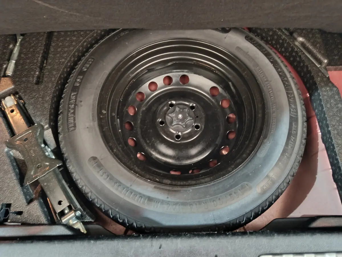 Gros plan sur la roue de secours noire et le cric dans le coffre du Renault Kadjar Intens rouge de 2017.