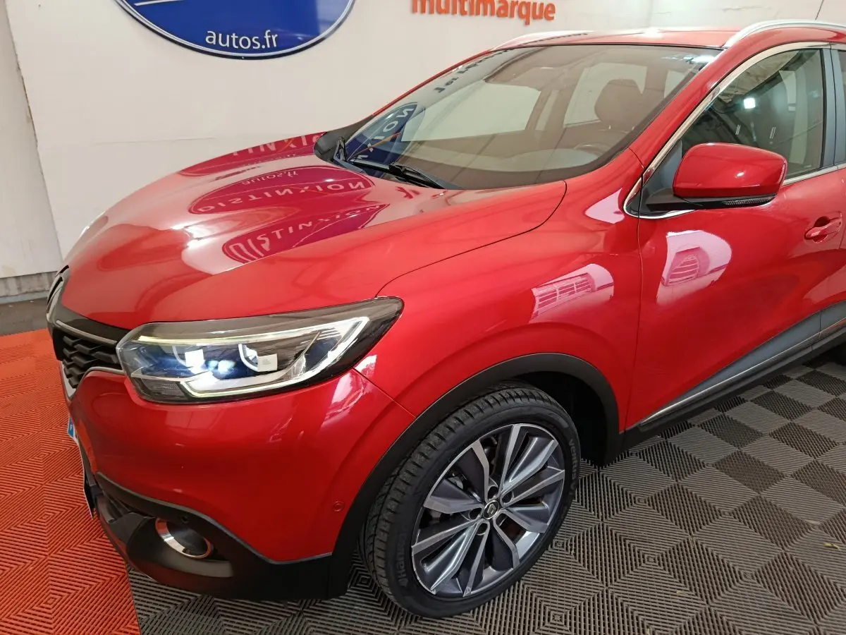 Vue 3/4 avant droite d'un Renault Kadjar Intens rouge avec phares LED allumés et jantes alliage visibles.