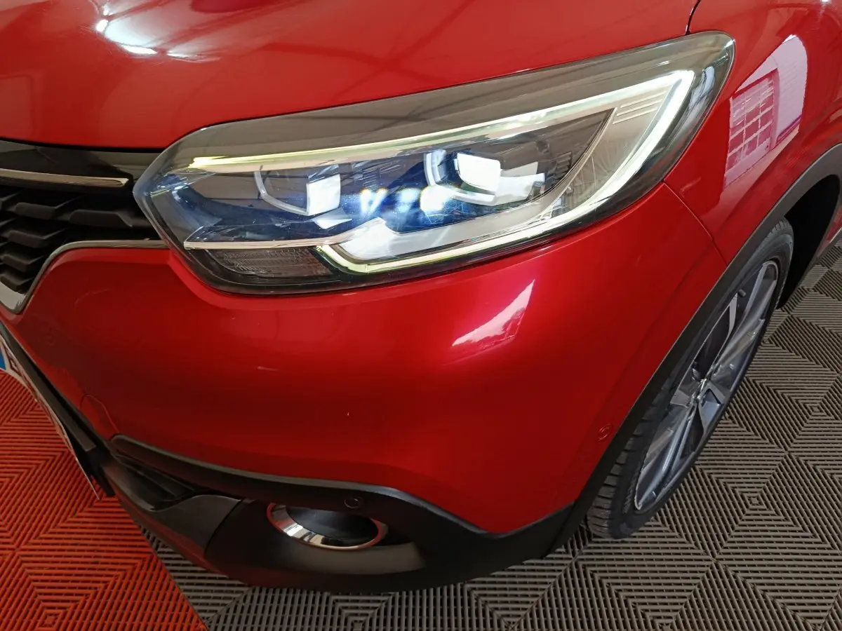 Gros plan sur le phare avant droit allumé d'un Renault Kadjar Intens rouge, avec partie de la calandre et roue visible.