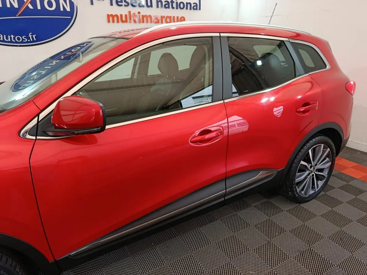 Profil côté gauche du Renault Kadjar rouge 2017 avec jantes alliage et rétroviseur assorti visible en intérieur showroom.
