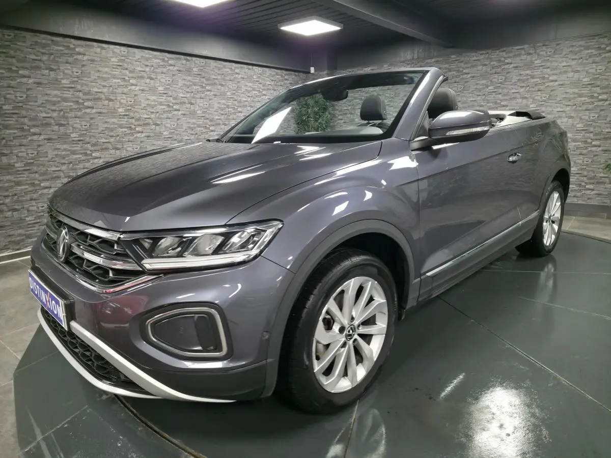 Volkswagen T-Roc Cabriolet gris métallisé en 3/4 avant droit, capote noire ouverte et jantes alliage visibles.
