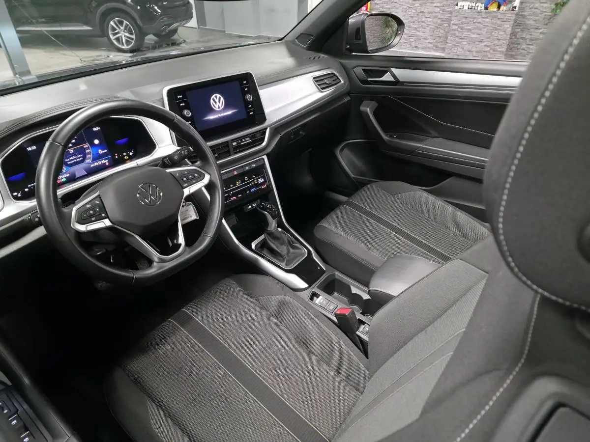 Intérieur avant du Volkswagen T-Roc 2024 avec sellerie tissu noire et tableau de bord numérique vu côté conducteur.