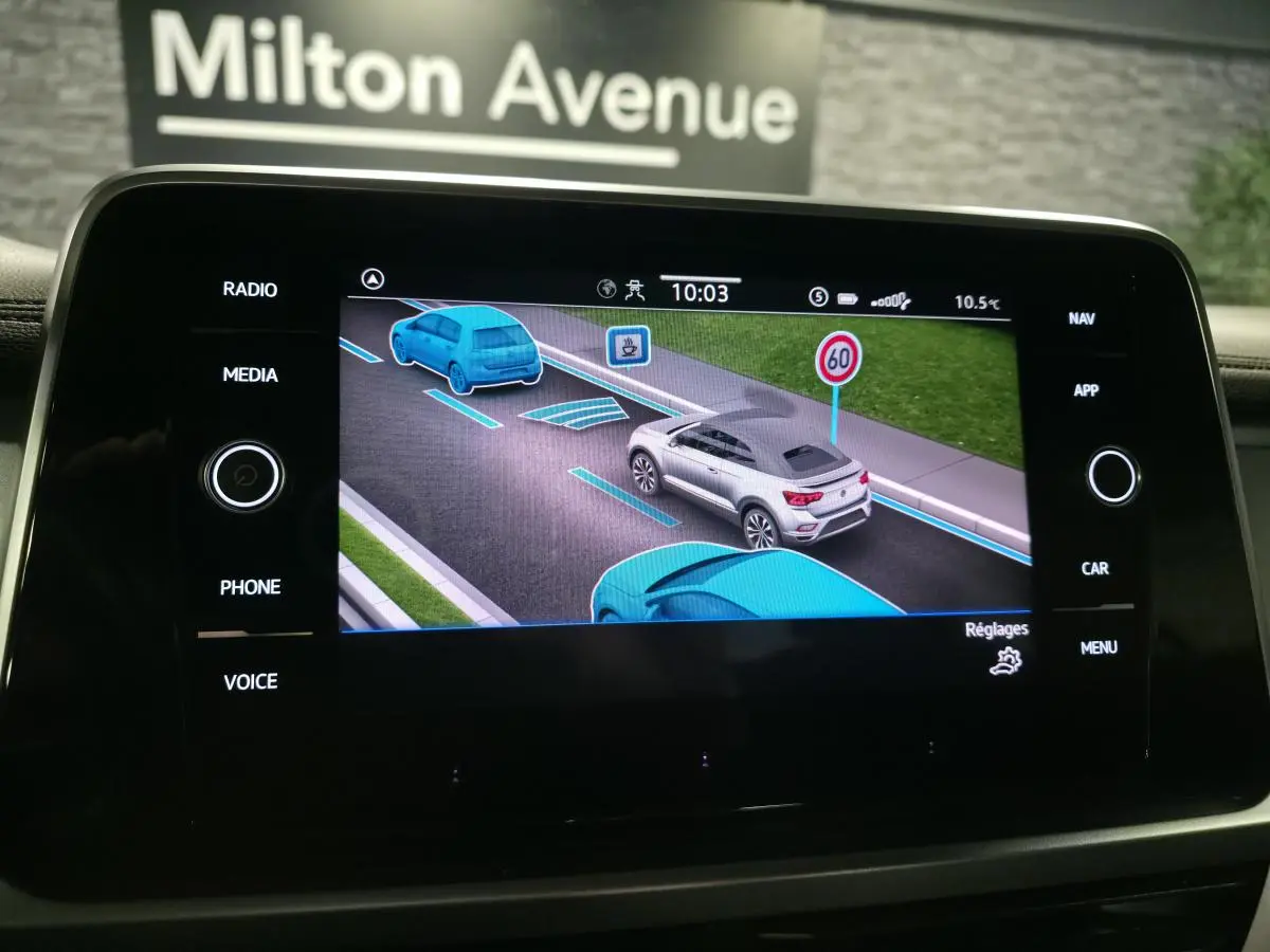Écran tactile intérieur montrant l'assistance de conduite avec un Volkswagen T-Roc gris vu de trois quarts arrière droit.