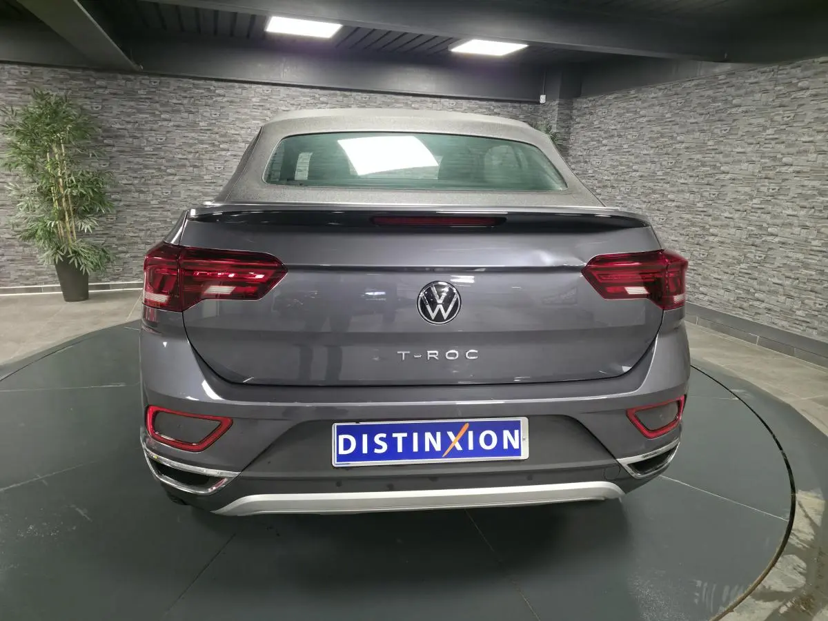 Vue arrière d'un Volkswagen T-Roc cabriolet gris métallisé avec capote textile grise dans un showroom.