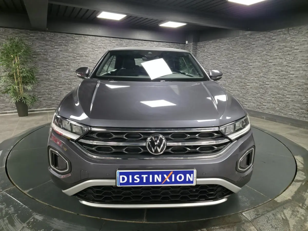 Vue frontale d'un Volkswagen T-Roc Cabriolet gris métallisé 2024 avec calandre chromée et plaque Distinxion.