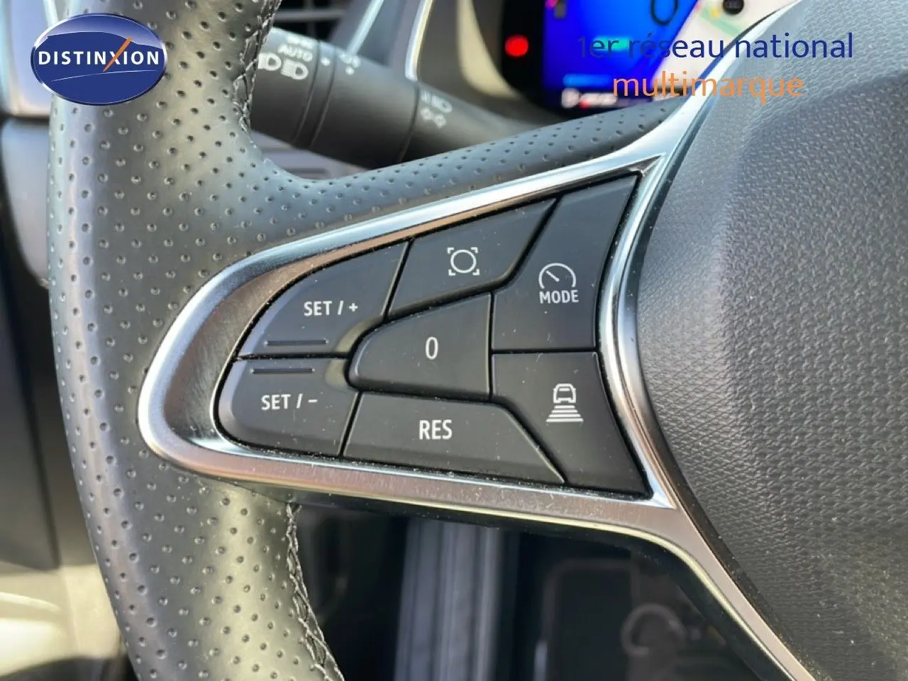 Gros plan sur les commandes au volant en cuir perforé du Renault Symbioz gris cassiopée, avec boutons de régulateur et mode.