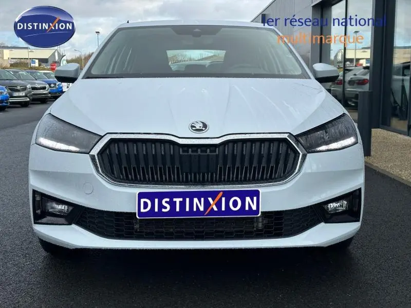Vue frontale d'une Skoda Fabia 2024 blanche avec calandre noire et phares LED allumés sur parking.