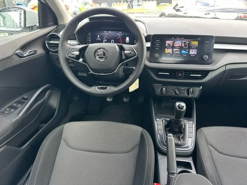 Intérieur de la Skoda Fabia 2024 en tissu gris, vue frontale du poste de conduite avec volant cuir et écran tactile central.