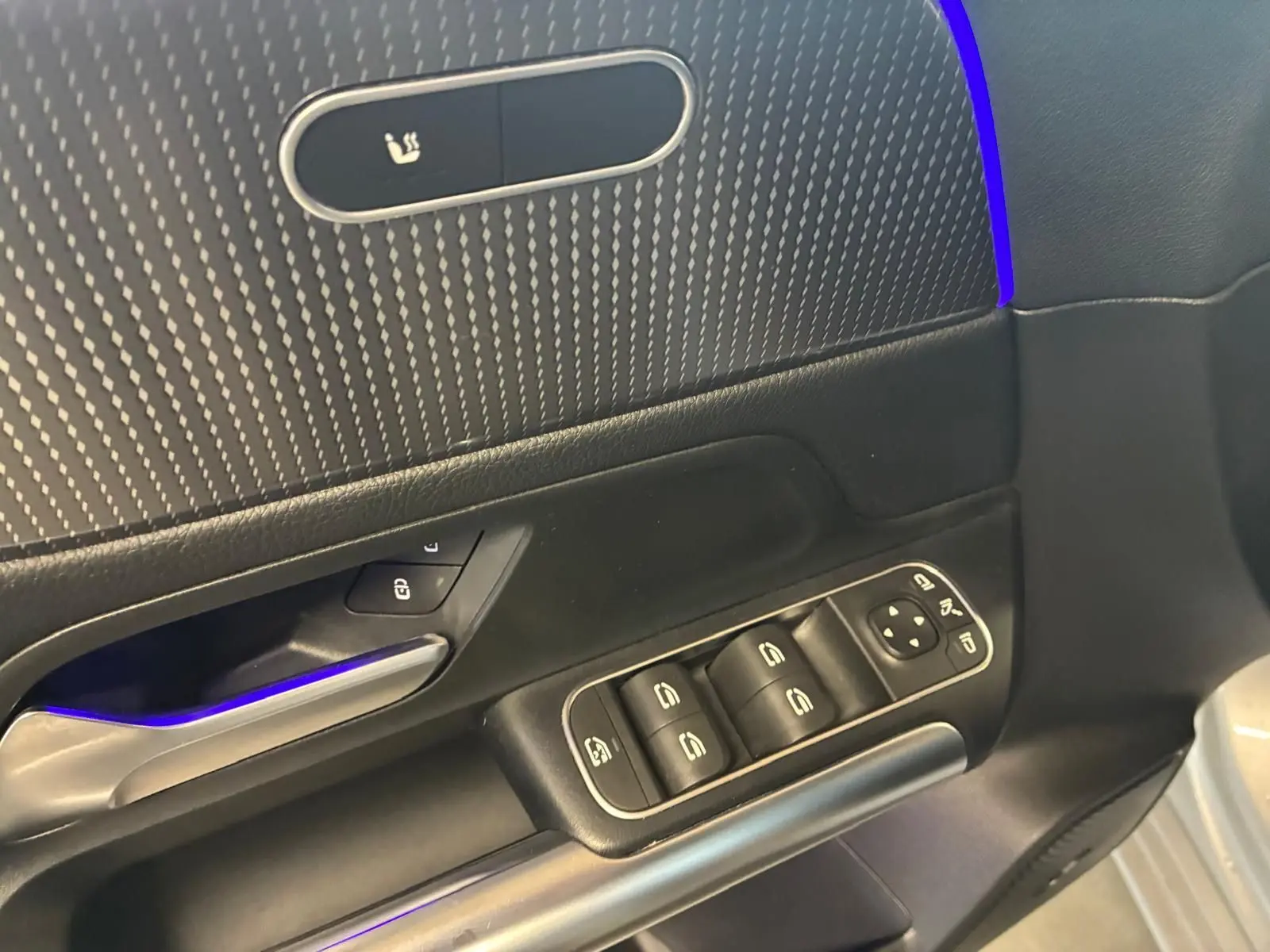 Détail de la porte côté conducteur d'une Mercedes Classe B 200D gris, avec commandes électriques et éclairage d'ambiance bleu.