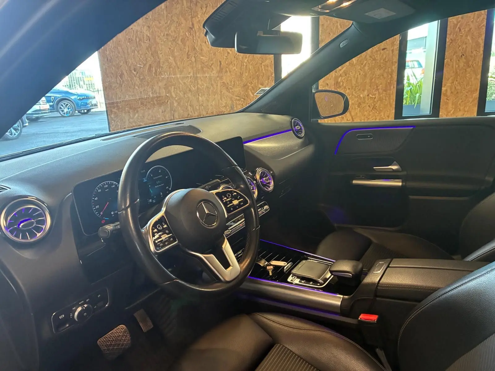 Intérieur avant droit d'une Mercedes Classe B 200D gris, volant multifonctions et éclairage d'ambiance violet visible.