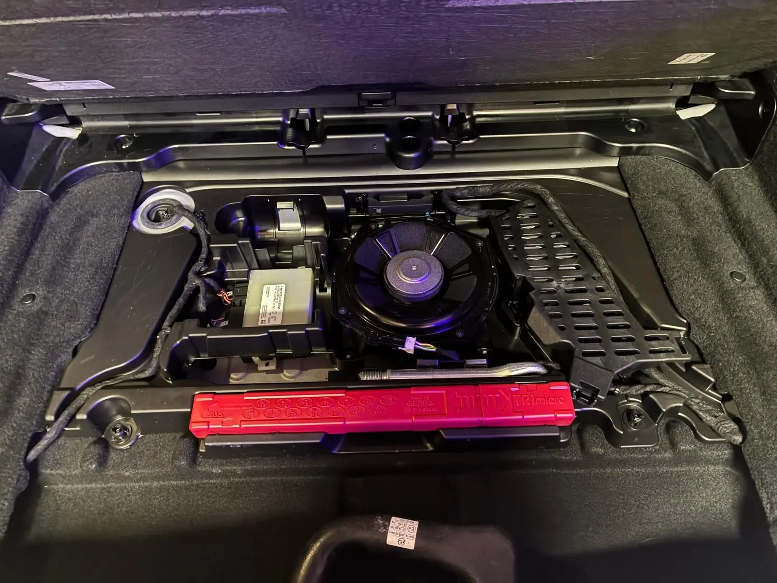 Vue rapprochée du compartiment de rangement sous le coffre d’une Mercedes Classe B 200D gris, montrant les outils et équipements d’origine.