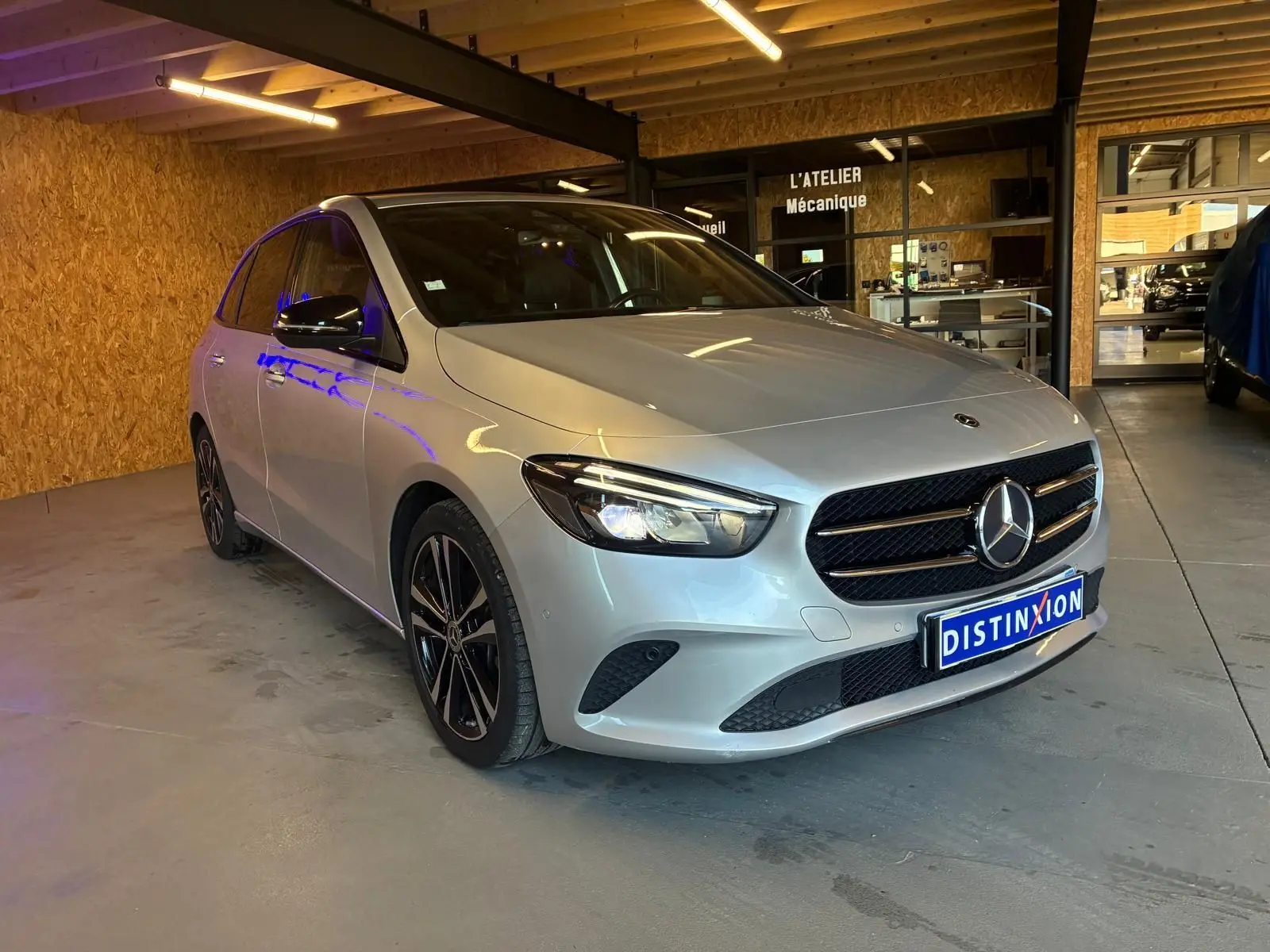 Mercedes Classe B 200D Progressive Line gris vue 3/4 avant droit dans un garage avec éclairage intérieur.