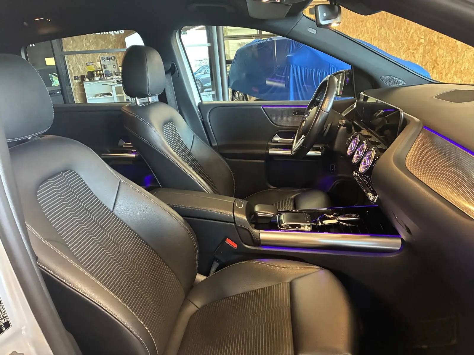 Vue intérieure côté droit de la Mercedes Classe B 200D Progressive Line 2019 avec sièges tissu gris et éclairage d’ambiance violet.