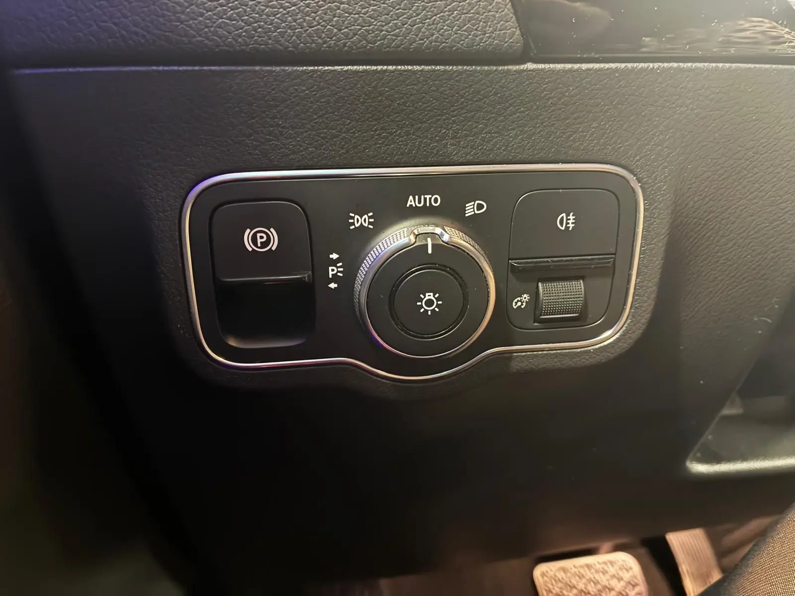 Gros plan sur le panneau de commande des phares et du frein à main électrique dans l’habitacle gris-noir d’une Mercedes Classe B 200D Progressive Line.