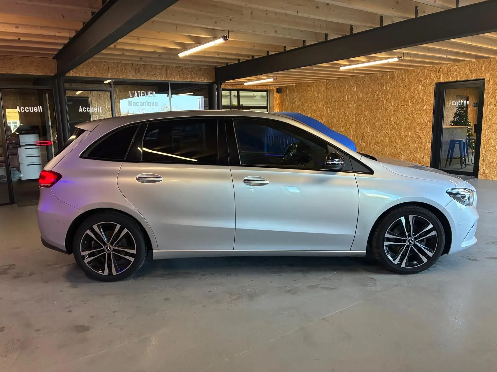 Vue de profil côté gauche d'une Mercedes Classe B 200D Progressive Line gris métallisé, avec jantes alliage et vitres teintées.