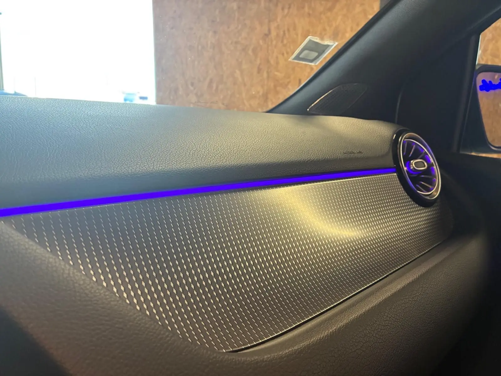 Détail de la planche de bord gris foncé de la Mercedes Classe B 200D avec éclairage d'ambiance bleu et sortie d'air ronde.