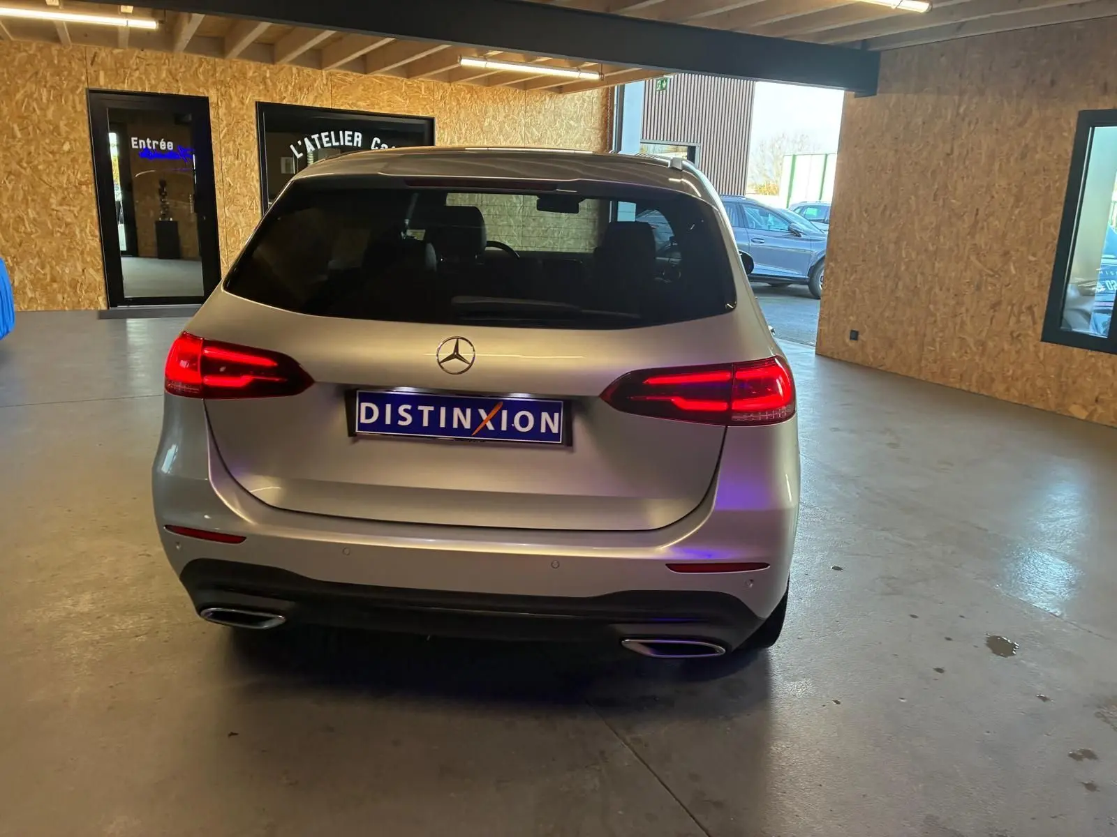 Vue arrière d'une Mercedes Classe B 200D Progressive Line gris, feux arrière allumés dans un garage.