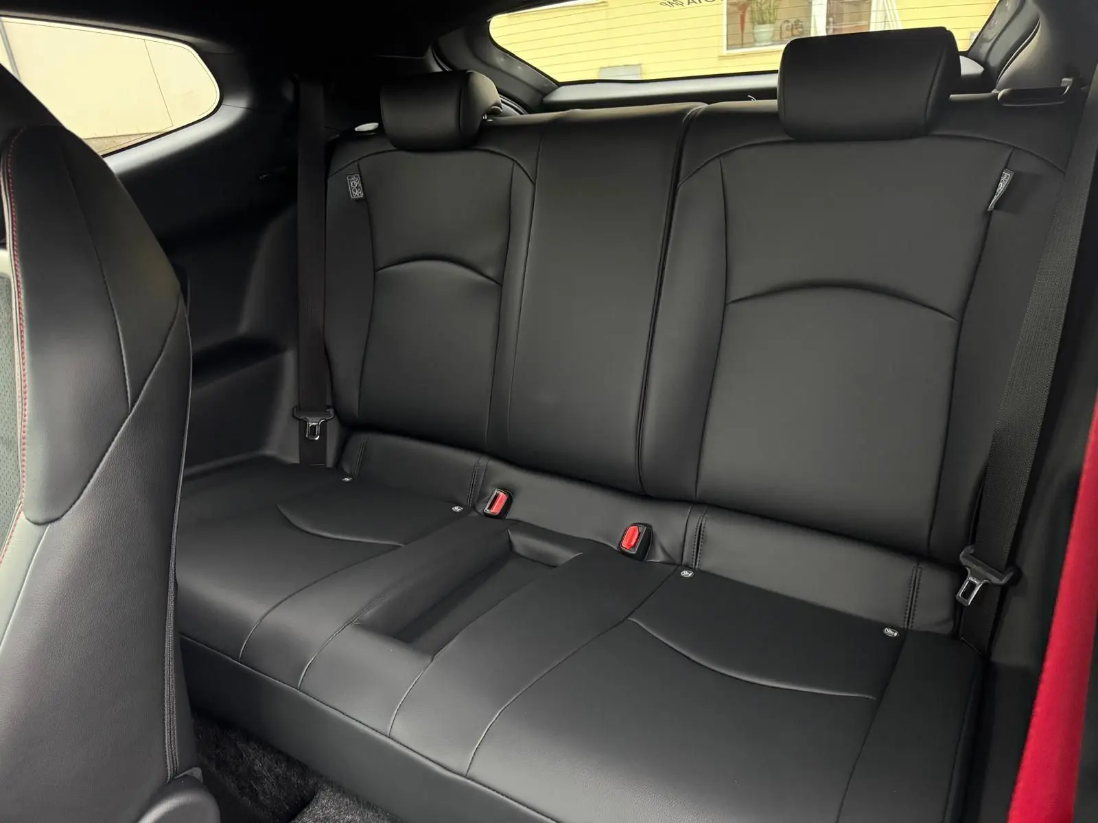 Vue intérieure de la banquette arrière en cuir noir de la Toyota Yaris GR avec ceintures de sécurité et surpiqûres rouges.