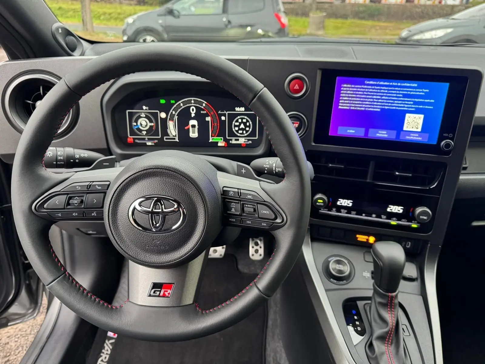 Vue intérieure centrée sur le volant Toyota Yaris GR avec surpiqûres rouges et écran tactile du tableau de bord.