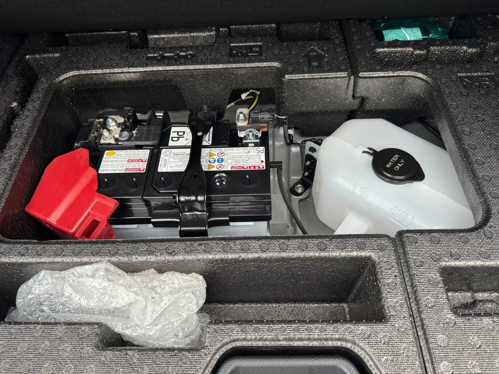 Gros plan sur la batterie et le réservoir d'eau sous le coffre d'une Toyota Yaris GR Pack Techno, compartiment en mousse noire.