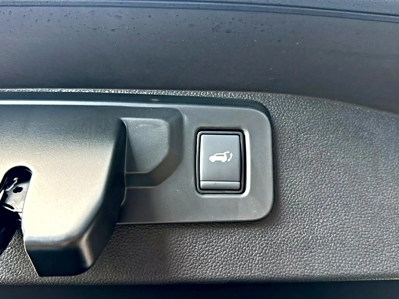 Gros plan sur le bouton d'ouverture électrique du coffre, intérieur noir texturé du Renault Austral bleu outremer.
