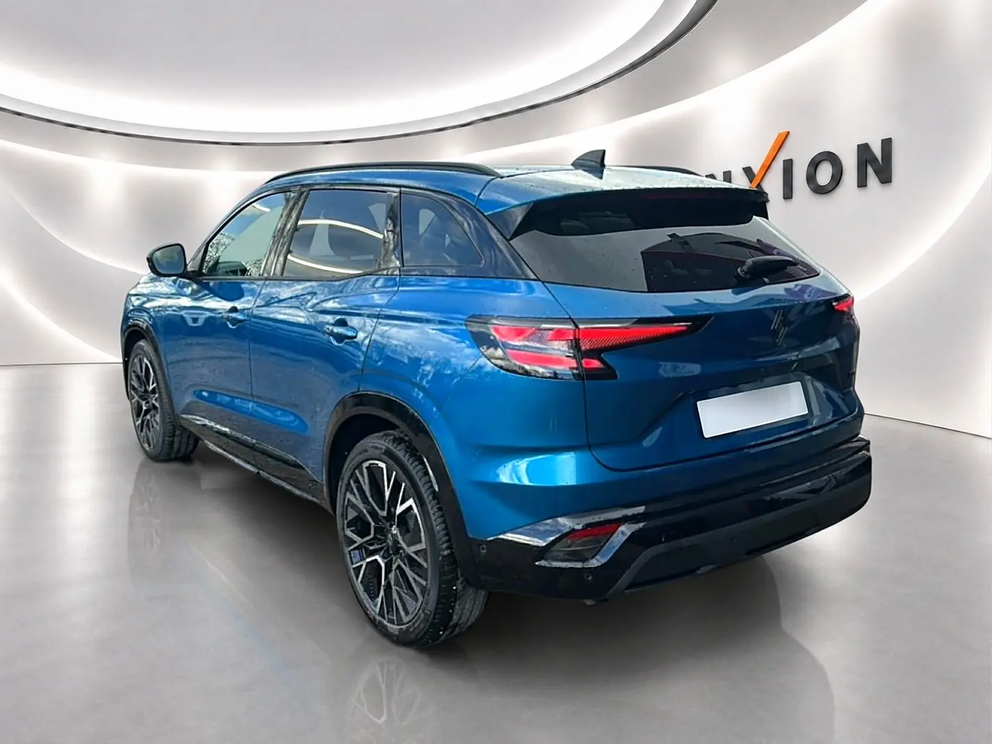 Vue 3/4 arrière droite d'un Renault Austral bleu outremer avec jantes alliage et toit noir dans un showroom lumineux.