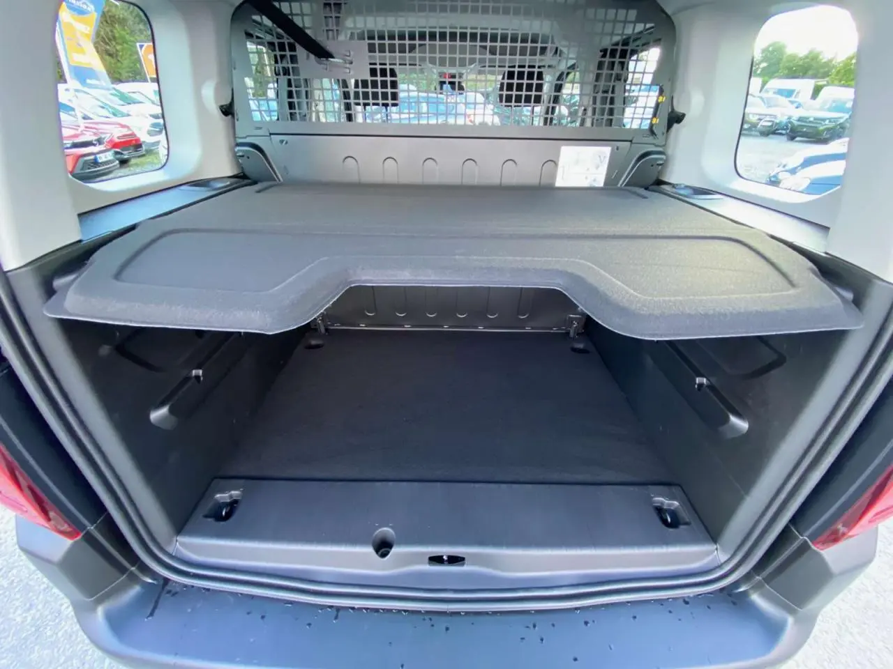 Vue arrière du coffre ouvert d'un Citroën Berlingo bleu 2025, montrant la séparation intérieure et la grille de protection.