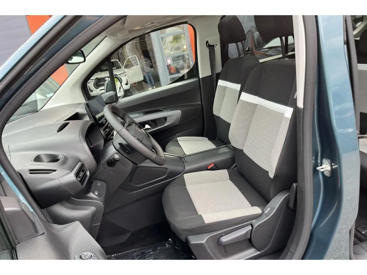 Vue intérieure côté conducteur du Citroën Berlingo bleu 2025, sièges bicolores gris et noir, tableau de bord moderne.