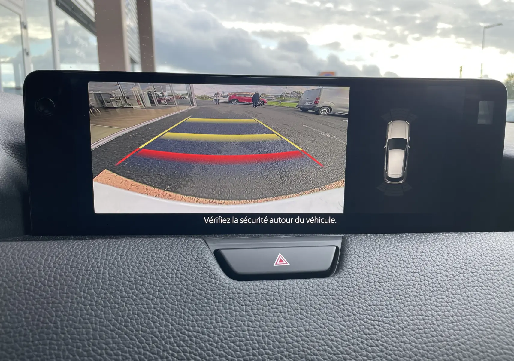 Écran intérieur du Mazda CX-60 blanc nacré montrant la caméra de recul avec lignes de guidage colorées et vue 360° du véhicule.