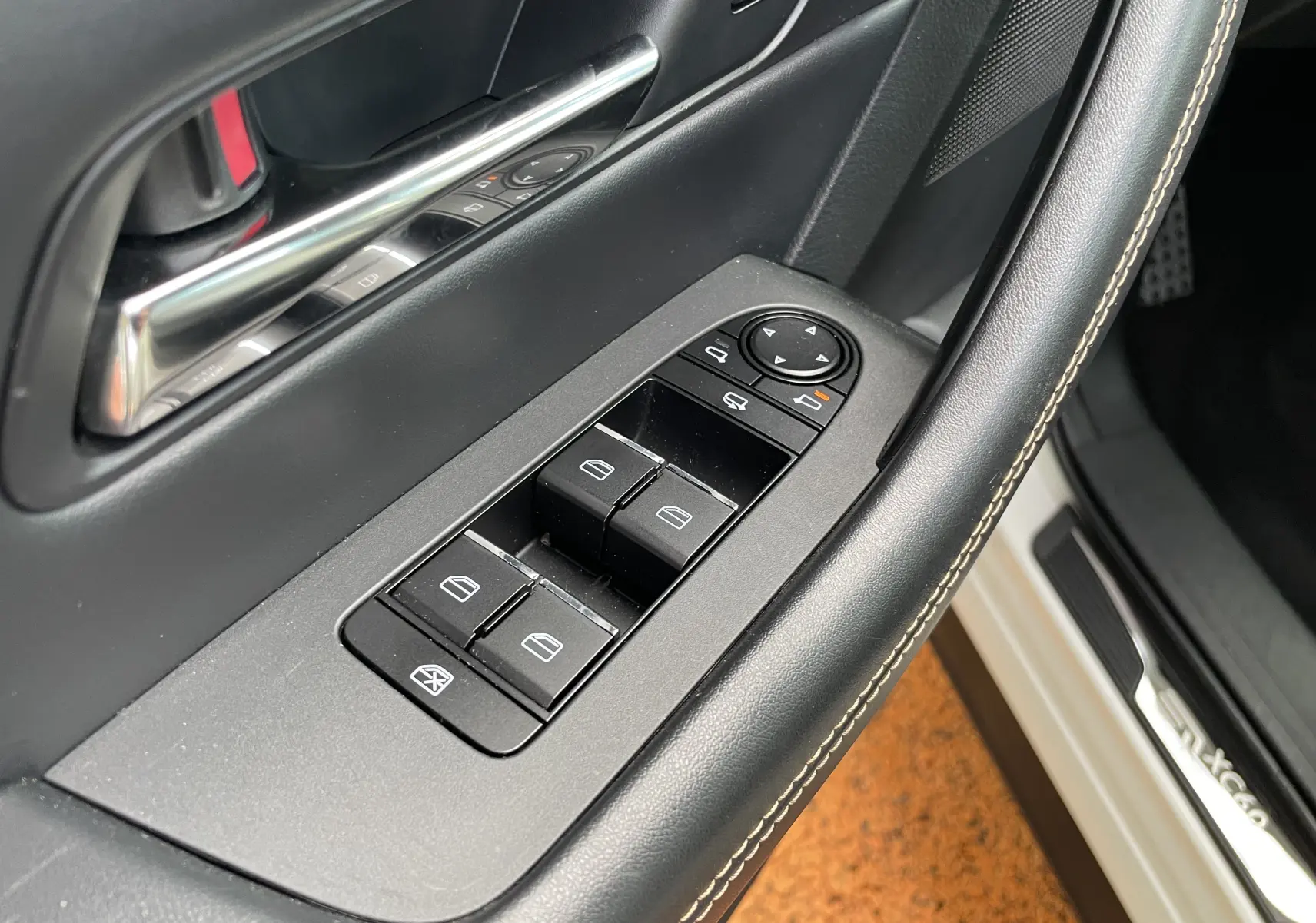 Gros plan sur la commande des vitres côté conducteur du Mazda CX-60 blanc nacré, avec poignée de porte et seuil visible.