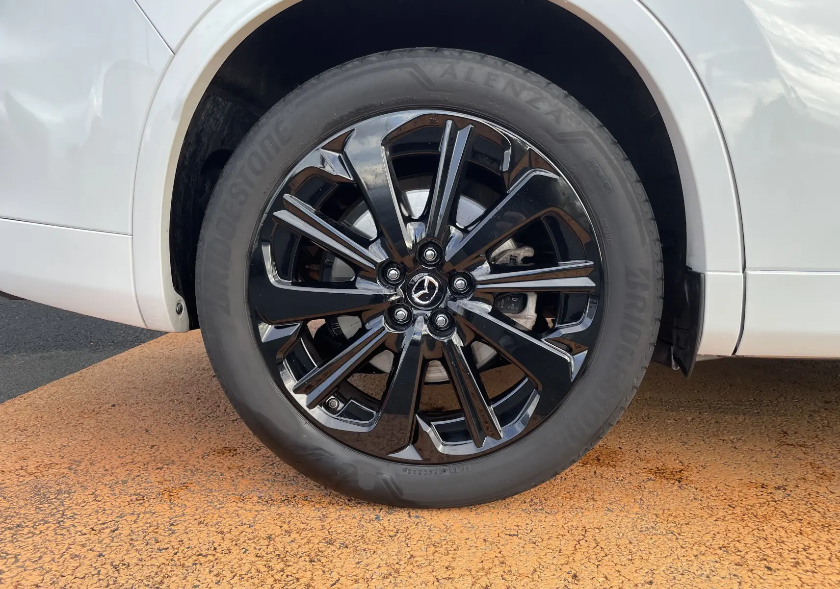 Gros plan sur la roue avant droite noire brillante du Mazda CX-60 blanc nacré, mettant en valeur la jante au design moderne.