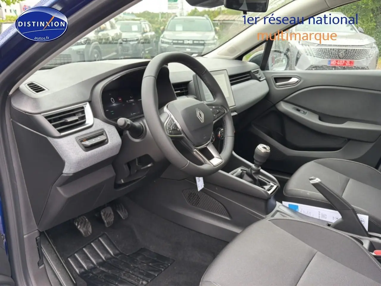 Intérieur avant droit de la Renault Clio V bleu iron, volant multifonction et boîte manuelle visibles.