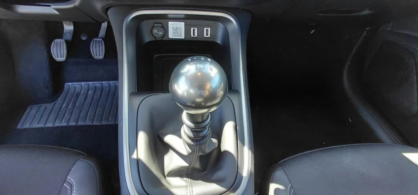 Vue rapprochée du levier de vitesses manuel noir du Jeep Avenger blanc 2025, avec pédales et console centrale visibles.